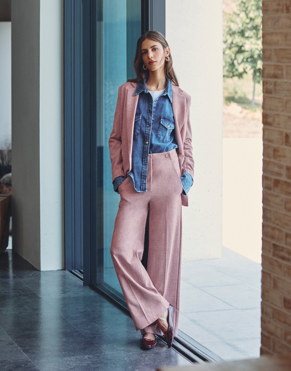 Donna in un completo rosa con camicia di jeans, sorridente e in piedi in un ambiente urbano