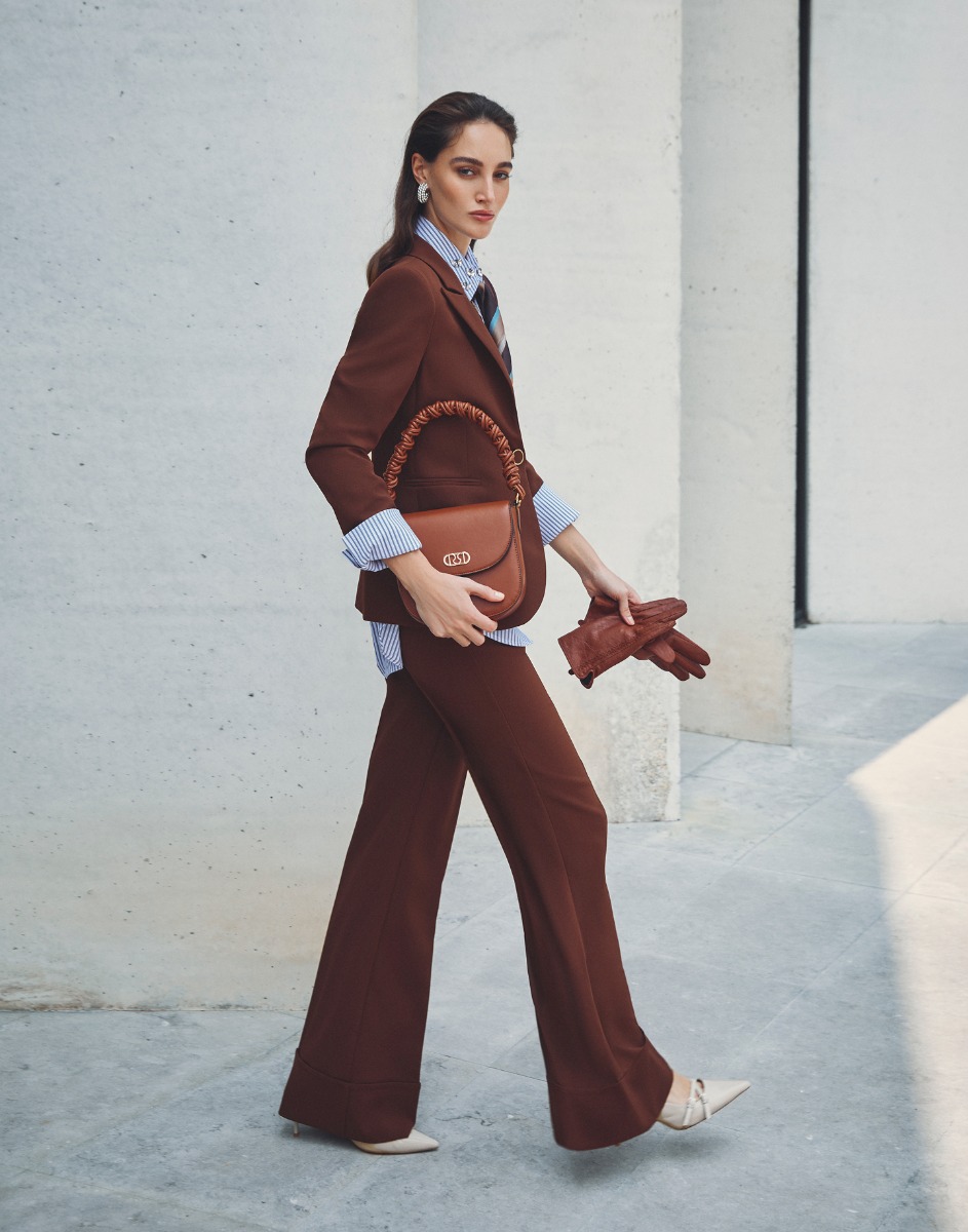 Donna vestita con un elegante abito marrone e scarpe coordinate, sorridente in un contesto formale