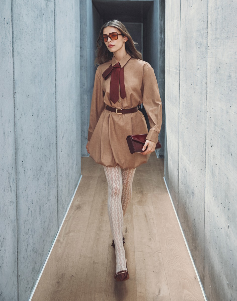 Donna in un vestito beige con una cravatta rossa, in piedi con un'espressione seria