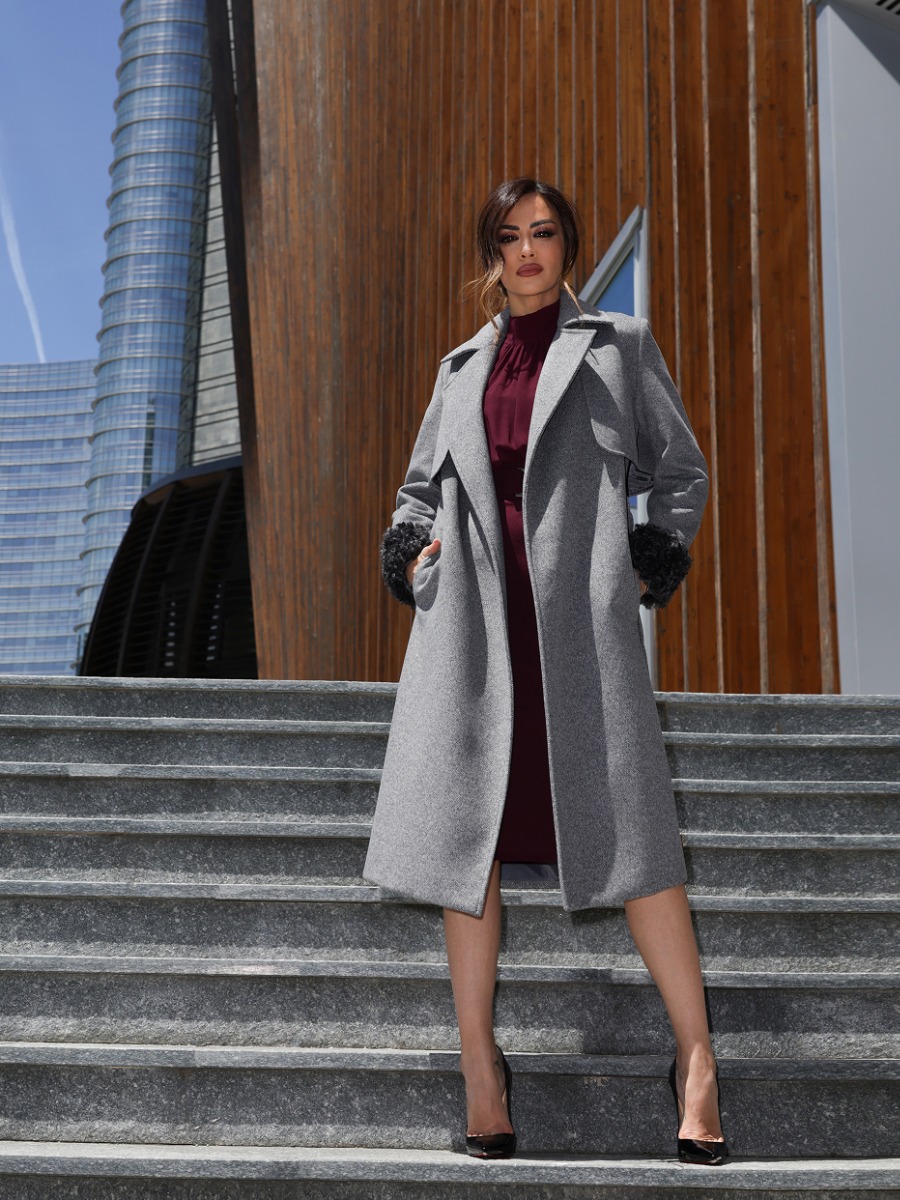 Giorgia Palmas in cappotto e vestito, in piedi su una scalinata, con un'espressione serena e un atteggiamento elegante