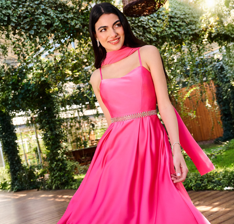 Una donna elegante in abito rosa, sorridente mentre posa per l'immagine.